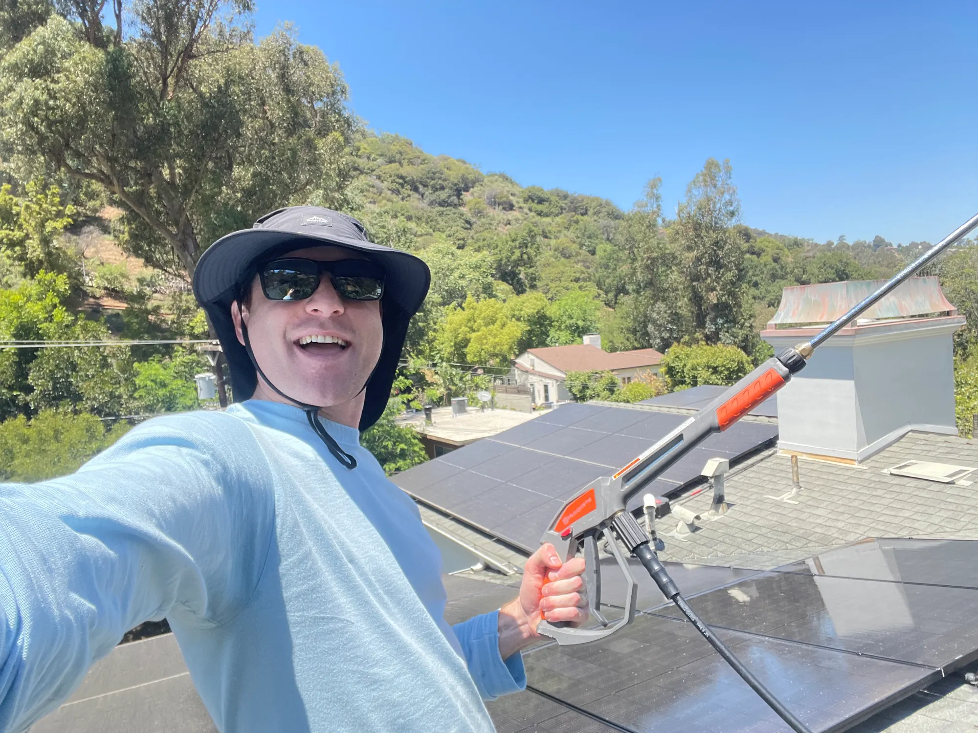 Logan in a bucket hat and sunglasses, wand in hand, on a rooftop with solar panels in the LA hills