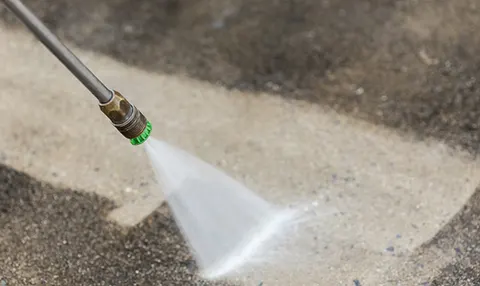 High-pressure nozzle cutting through grime on concrete